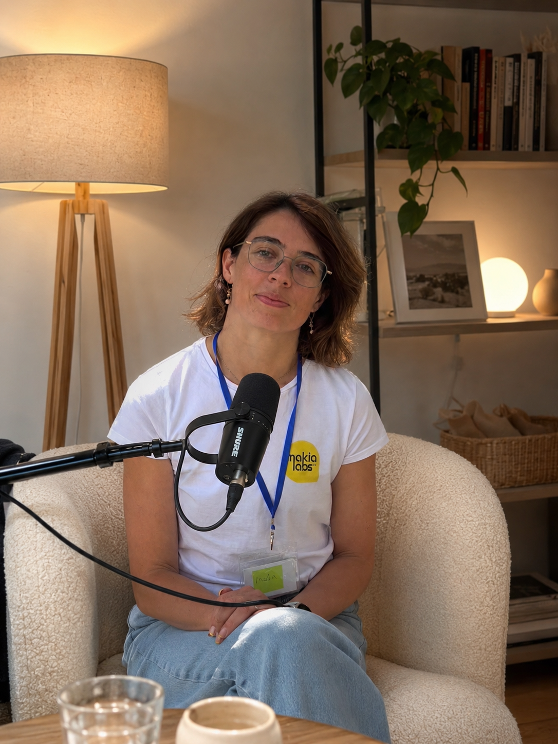 Maria seated in an armchair behind a podcast microphone, recording an episode in a warm living room